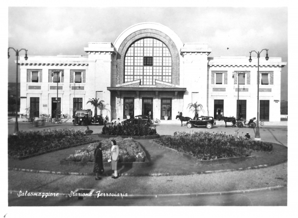 Stazione della Ferrovia - Collezione Biblioteca Comunale G. D. Romagnosi: La grande aiuola davanti alla stazione, sullo sfondo le carrozze a cavallo (riproduzione d'epoca)